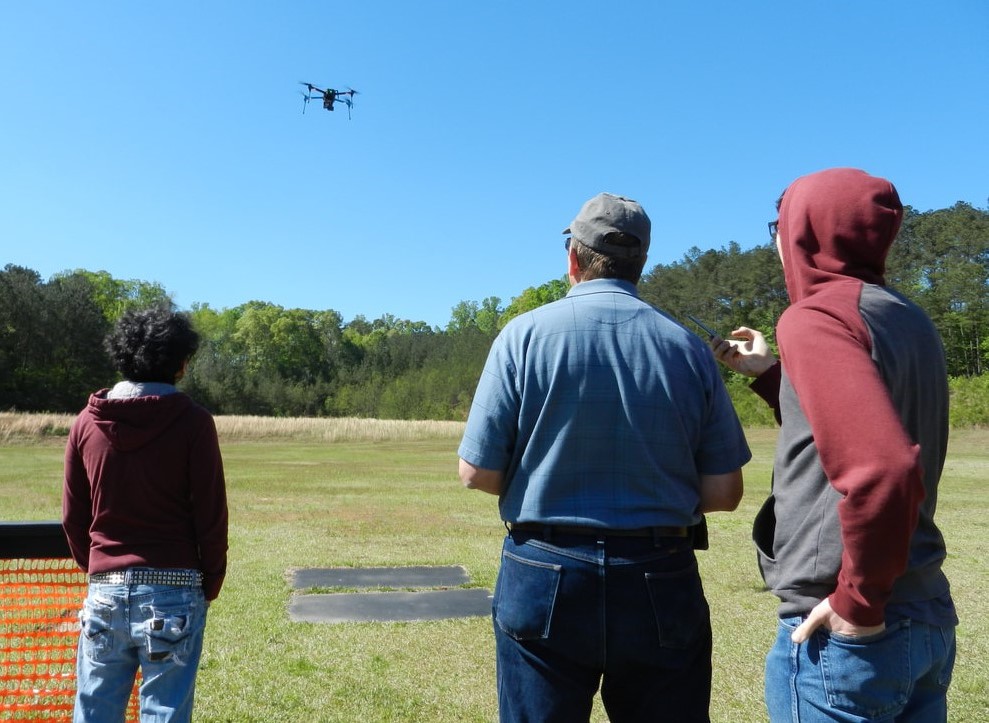 A drone piloted by one of three men in a field