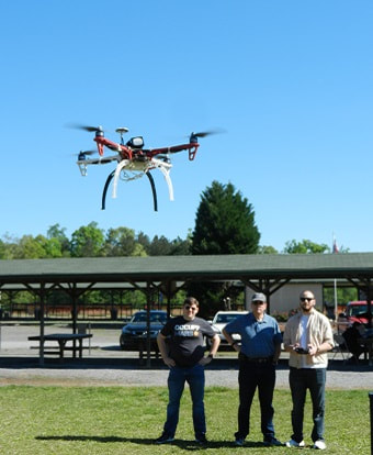 Drone being piloted by one of three men in a field
