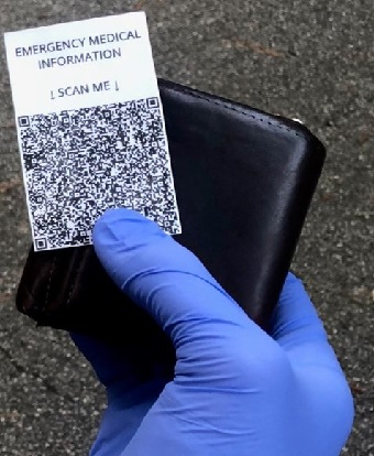 Gloved hand holding a wallet and a card with a QR labeled Emergency Medical Information SCAN ME